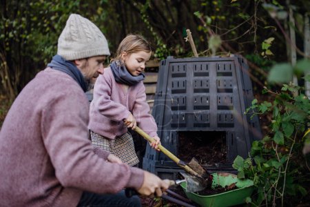 Foto de Chica ayudando a padre a eliminar el compost del compostador en el jardín. Concepto de compostaje y jardinería orgánica sostenible. - Imagen libre de derechos