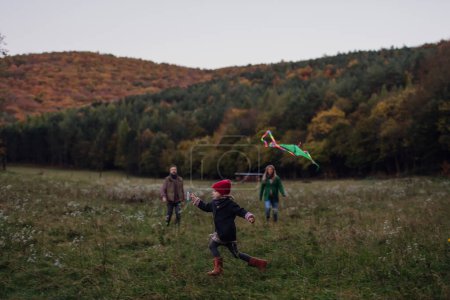 Téléchargez les photos : Fille volant un cerf-volant sur prairie, courir, s'amuser avec les parents. Météo automnale venteuse pour le cerf-volant. - en image libre de droit