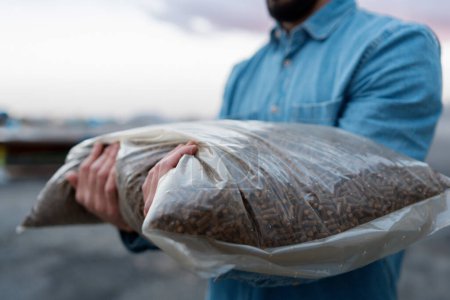Photo for Man holding bag with wood pellets, pellet fuels manufactured in wood pellet line. Reusing wooden industrial waste, sawdust. - Royalty Free Image