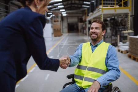 Téléchargez les photos : Homme en fauteuil roulant travaillant dans un entrepôt, serrant la main du directeur des RH, directeur. Concept de travailleurs handicapés, lieu de travail accessible pour les employés à mobilité réduite. - en image libre de droit