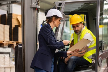 Photo for Male forklift driver talking with manager in modern industrial factory. Warehouseman reading order, order picking. Warehouse worker preparing products for shipmennt, delivery, checking stock in - Royalty Free Image