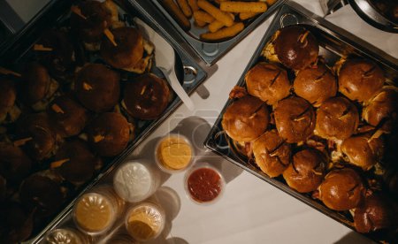 Foto de Placa con hamburguesas para fiesta, con lados y salsas. Servir hamburguesas y comida rápida en la boda. - Imagen libre de derechos