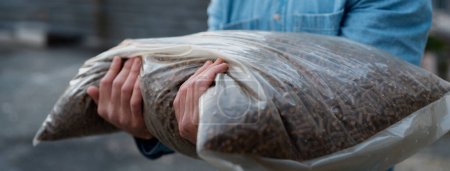Téléchargez les photos : Homme tenant sac avec granulés de bois, granulés de bois fabriqués dans la ligne de granulés de bois. Réutilisation des déchets industriels en bois, sciure de bois. - en image libre de droit