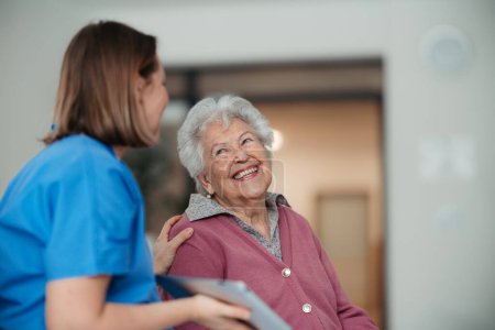 Retrato de enfermera y paciente mayor que habla en el pasillo del hospital. Apoyo emocional para la mujer anciana.