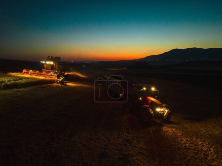 Foto de Vista aérea de un tractor una cosechadora que trabaja en el campo durante la noche. Agricultura y cultivo de granjas industriales. Agroindustria. - Imagen libre de derechos