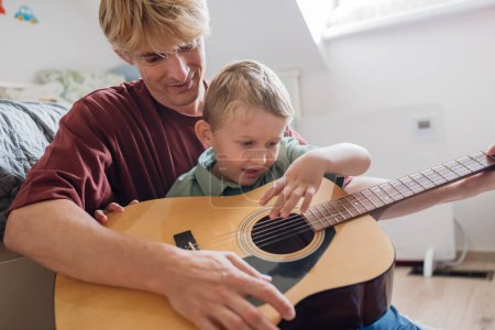 Téléchargez les photos : Père apprenant à jouer de la guitare. Fils s'amuser dans leur chambre avec papa, jouer de la guitare et chanter. Concept de la Journée des Pères, et amour paternel. - en image libre de droit