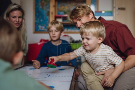 Photo for Cheerful family with three kids playing in kids room. Family board game, playtime, having fun together. Air hockey table. - Royalty Free Image