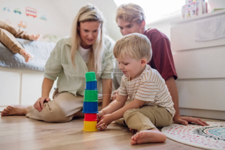Photo for Parents looking at little boy building a tower in childrens room. Stacking blocks, building game for the preschooler. - Royalty Free Image