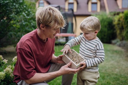 Téléchargez les photos : Père avec un petit fils faisant un hôtel insecte, ou une maison d'insectes à l'extérieur dans le jardin. Garçon en apprendre davantage sur les insectes, l'écosystème du jardin et la biodiversité. - en image libre de droit