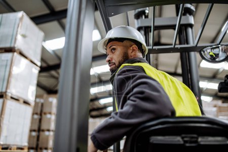 Photo for Portrait of multiracial warehouse worker driving forklift. Warehouse worker preparing products for shipmennt, delivery, checking stock in warehouse. - Royalty Free Image