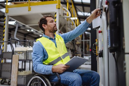 Man in wheelchair working in modern industrial factory, in adjustable workstation. Concept of workers with disabilities, accessible workplace for employees with mobility impairment.
