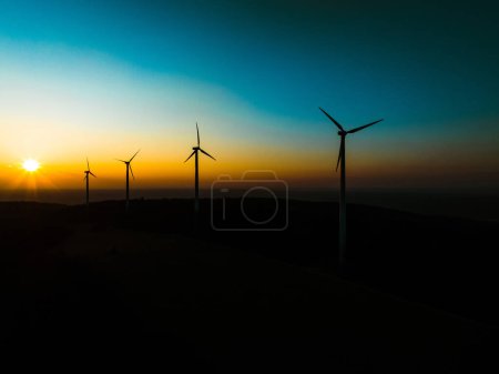 Téléchargez les photos : Photographie aérienne de paysage du lever du soleil sur la nature avec des éoliennes. L'éolienne domine en douce lumière du matin avec forêt, arbres autour, harmonie de la nature et de la technologie. Concept d'énergie éolienne comme - en image libre de droit