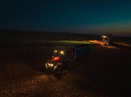 Foto de Vista aérea de un tractor una cosechadora que trabaja en el campo durante la noche. Agricultura y cultivo de granjas industriales. Agroindustria. - Imagen libre de derechos