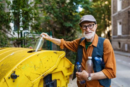 Téléchargez les photos : Homme âgé jetant des déchets plastiques, bouteilles dans un conteneur de recyclage en face de son appartement. Homme âgé triant les déchets selon le matériau dans des poubelles colorées. - en image libre de droit