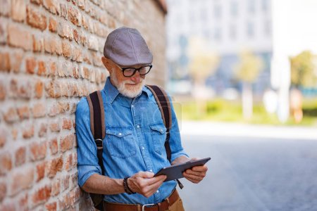 Photo for Side view of senior tourist exploring a new city, interesting places. Elderly man holding tablet, looking for the route. Traveling and solo trips in retirement. - Royalty Free Image