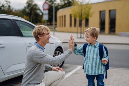 Photo for Father saying goodbyeto to his son in front of school building, high five each other. Dad heading to work. Concept of work-life balance for parents. - Royalty Free Image