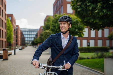 Téléchargez les photos : Un bel homme d'âge moyen qui se déplace dans la ville à vélo en costume noir. Navetteur urbain masculin voyageant du travail à vélo après une longue journée de travail. - en image libre de droit