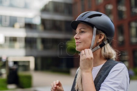 Téléchargez les photos : Belle femme d'âge moyen qui se déplace à travers la ville en vélo. Femme banlieue de la ville voyageant du travail à vélo après une longue journée de travail. - en image libre de droit