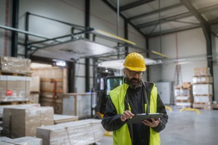 Photo for Warehouse receiver, clark standing by delivered cargo, holding tablet, looking at cargo details, checking delivered items, goods against order. - Royalty Free Image