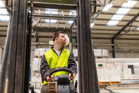 Young man with Down syndrome driving forklift in factory, warehouse. Concept of workers with disabilities, support in workplace.