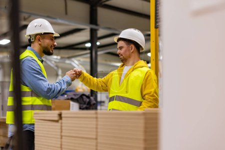Photo for Young man with Down syndrome working in modern factory, fist bump with colleague, teamwork.. Concept of workers with disabilities, support in the workplace. - Royalty Free Image