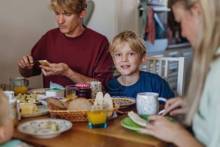 Photo for Young family eating breakfast together in home kitchen. Healty breakfast or snack before school and work. - Royalty Free Image