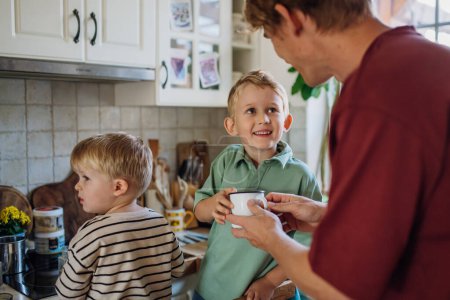 Téléchargez les photos : Famille préparant le petit déjeuner dans la cuisine de la maison le matin. Passer du temps ensemble avant d'aller à l'école et de travailler. - en image libre de droit