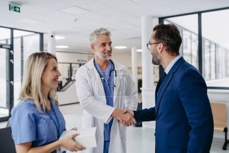 Pharmaceutical sales representative talking with doctors in medical building, shaking hands. Drug rep presenting new pharmaceutical product, drug. Hospital director, manager in private medical clinic