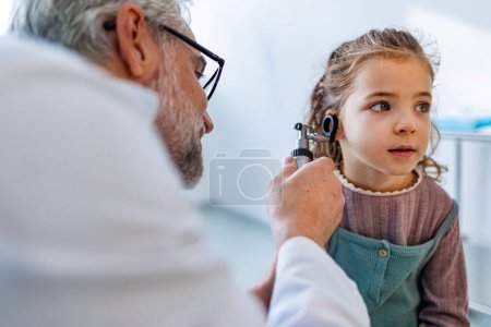Nahaufnahme eines Arztes, der kleine Mädchen mittels Otoskop im Ohr untersucht und nach Infektionen sucht. Freundschaftliche Beziehung zwischen Arzt und Patient.