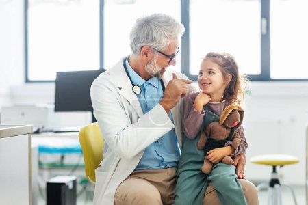 Photo for Portrait of a pediatrician with a little girl patient sitting on his knee. Friendly relationship between the doctor and the child patient. - Royalty Free Image