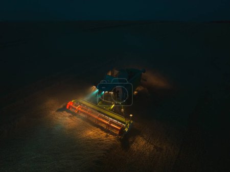 Téléchargez les photos : Vue aérienne d'un tracteur une moissonneuse travaillant sur le terrain pendant la nuit. Agriculture et culture des exploitations industrielles. Agro-alimentaire. - en image libre de droit