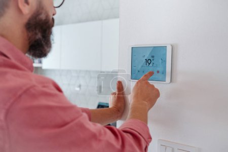 Téléchargez les photos : Homme utilisant thermostat intelligent, réglage ou abaissement des températures de chauffage à sa maison. Concept de technologie durable, efficace et intelligente dans le chauffage domestique et les thermostats. - en image libre de droit