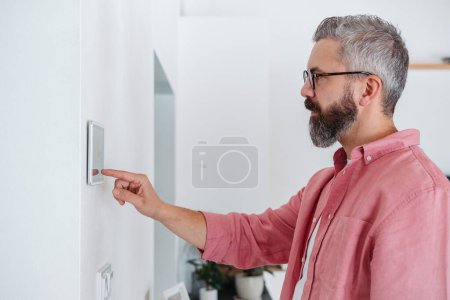 Mann benutzt intelligentes Thermostat, um die Heizungstemperaturen in seinem Haus anzupassen oder zu senken. Konzept nachhaltiger, effizienter und intelligenter Technologien in der Beheizung und Thermostaten von Haushalten.