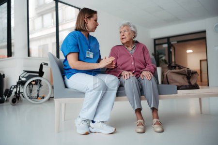 Téléchargez les photos : Portrait d'une infirmière soignante et d'une patiente âgée parlant dans un couloir d'hôpital. Soutien émotionnel pour les femmes âgées. - en image libre de droit