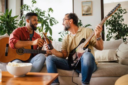 Photo for Best friends, musician jamming together. Playing music on acoustic and electric guitar together, having beer and fun. Concept of male friendship, bromance. - Royalty Free Image