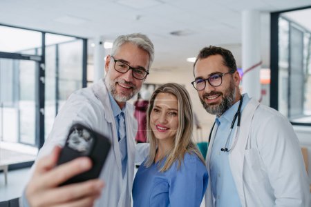 Foto de Retrato de médicos y enfermeras de pie en el pasillo del hospital. Trabajadores de la salud en la clínica privada moderna, tomando selfie y sonriendo. - Imagen libre de derechos