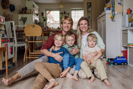 Foto de Retrato de la familia sentada en el suelo en la sala de estar. Hermosa madre con sus tres hijos y marido mirando a la cámara y sonriendo. - Imagen libre de derechos