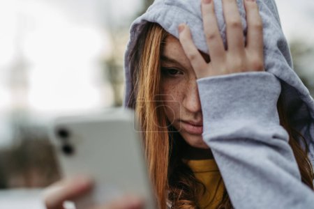 Téléchargez les photos : Portrait d'une adolescente regardant son smartphone, se sentant triste, anxieuse, seule. Cyberintimidation, fille est harcelée, trois en ligne. - en image libre de droit