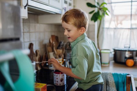 Téléchargez les photos : Garçon aider avec le petit déjeuner dans la cuisine à la maison le matin.Passer du temps ensemble avant d'aller à l'école et au travail. - en image libre de droit
