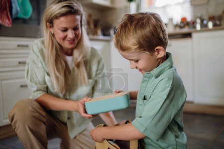 Photo for Mom is packing snack for her son for school. Putting lunch box with healthy snack into his school bag for lunch. - Royalty Free Image