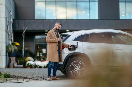 Photo for Man plugging in charging plug in electric car before going to shopping. An electric vehicle charging station in front of shop building, supermarket. Charging while shopping. - Royalty Free Image