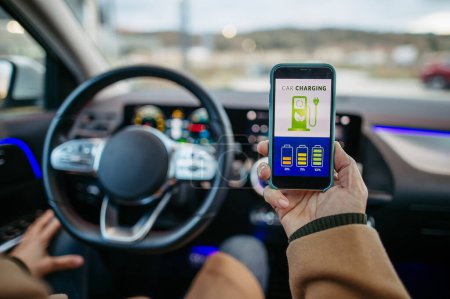 Photo for Close up of man using electric vehicle charging app, checking battery status, level on smart phone. Charging apps for monitoring electricity usage, locating charging stations. - Royalty Free Image