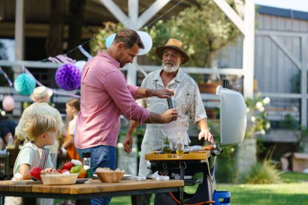 Photo for Young boy cutting vegetables for grilling. Father, grandfather and son grilling together at a garden bbq party. Three generations of men at summer family garden party. - Royalty Free Image