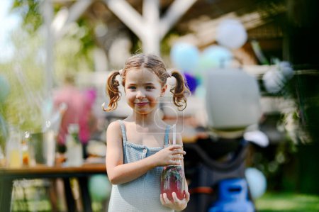 Foto de Linda niña aullando limonadas frescas en botella de vidrio. Fiesta de jardín de verano en el patio trasero. - Imagen libre de derechos