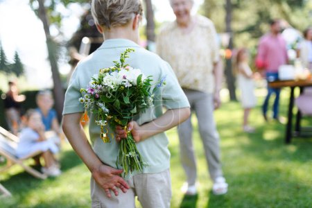 Photo for Beautiful senior birthday woman receiving flowers from grandson, grandchildren. Concept of garden birthday party for elderly woman. - Royalty Free Image