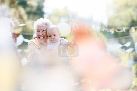 Foto de Retrato de la bisabuela sosteniendo a un pequeño bebé en sus brazos. Familia verano jardín partido. - Imagen libre de derechos