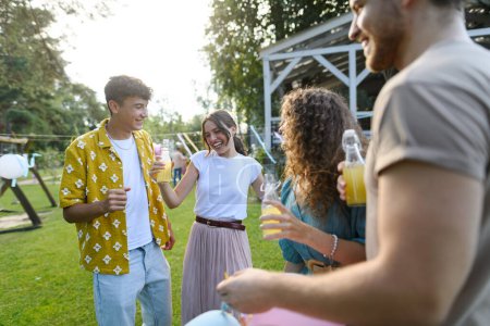 Téléchargez les photos : Les amis et la famille parlent et s'amusent lors d'une fête de jardin sur le gril d'été. Les gens à la fête dansent et rient, tenant des verres avec des boissons. - en image libre de droit