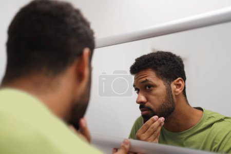 Téléchargez les photos : Beau homme se regardant dans le miroir, se sentant anxieux et déprimé le matin. Soin de routine pour jeune homme. - en image libre de droit