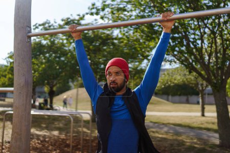 Photo for Handsome man exercises outdoors at an urban outdoor gym. Exercising after work for good mental health, physical health, and relieving stress and boost mood. The single man working out alone. - Royalty Free Image