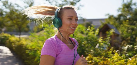 Photo for Young woman running outdoors and listening music. Exercising after work for good mental health, physical health, and relieving stress and boost mood. Banner with copy space. - Royalty Free Image